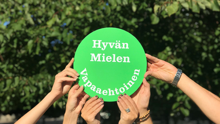 Monet kädet pitävät kylttiä: "Hyvän mielen vapaaehtoinen"