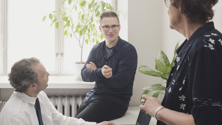 Kolme henkilöä juttelee iloisesti toimistohuoneessa