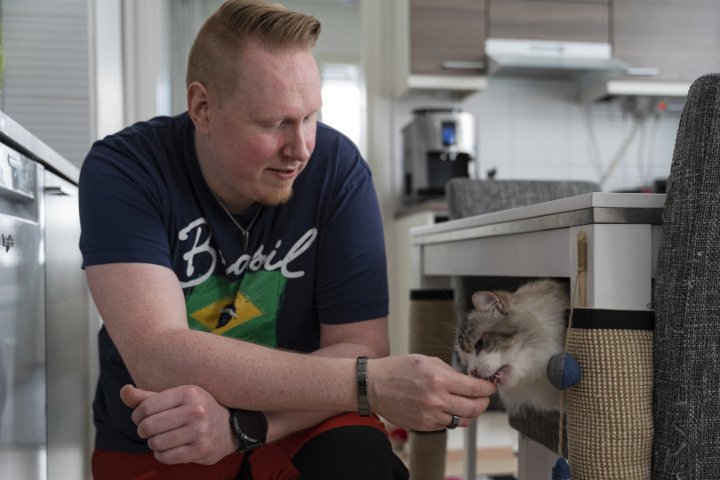 Pasi Ojala on kyykyssä lattialla ja syöttää kissaa.