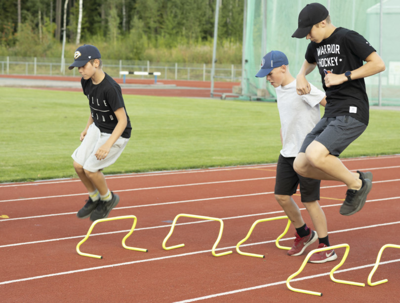 Nuoret hyppivät pikkuaitojen yli urheilukentällä