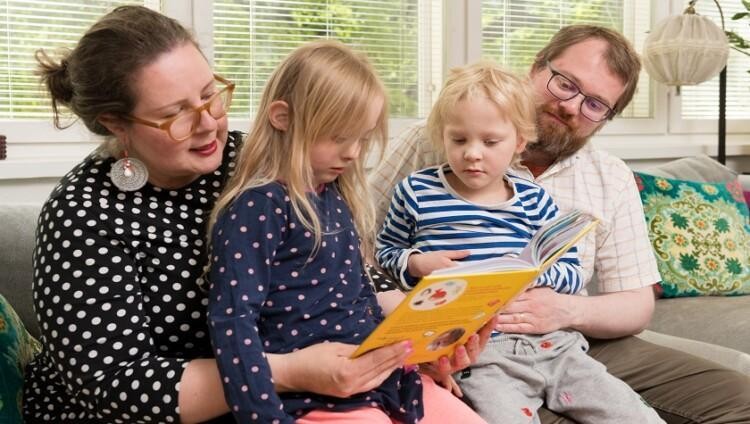 Mamma, pappa och två barn läser boken tillsammans.