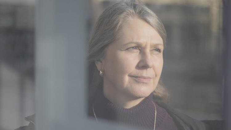 MIELI ry:n asiantuntija Marjo Lehtinen kuvattuna lasin läpi. Lehtinen katsoo kuvassa oikealle, kasvoilla vakava ilme.